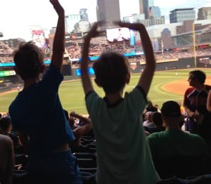 Two boys in silhouette cheer from the stands of a baseball game.