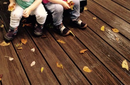 Four toddler feet on a damp deck with leaves